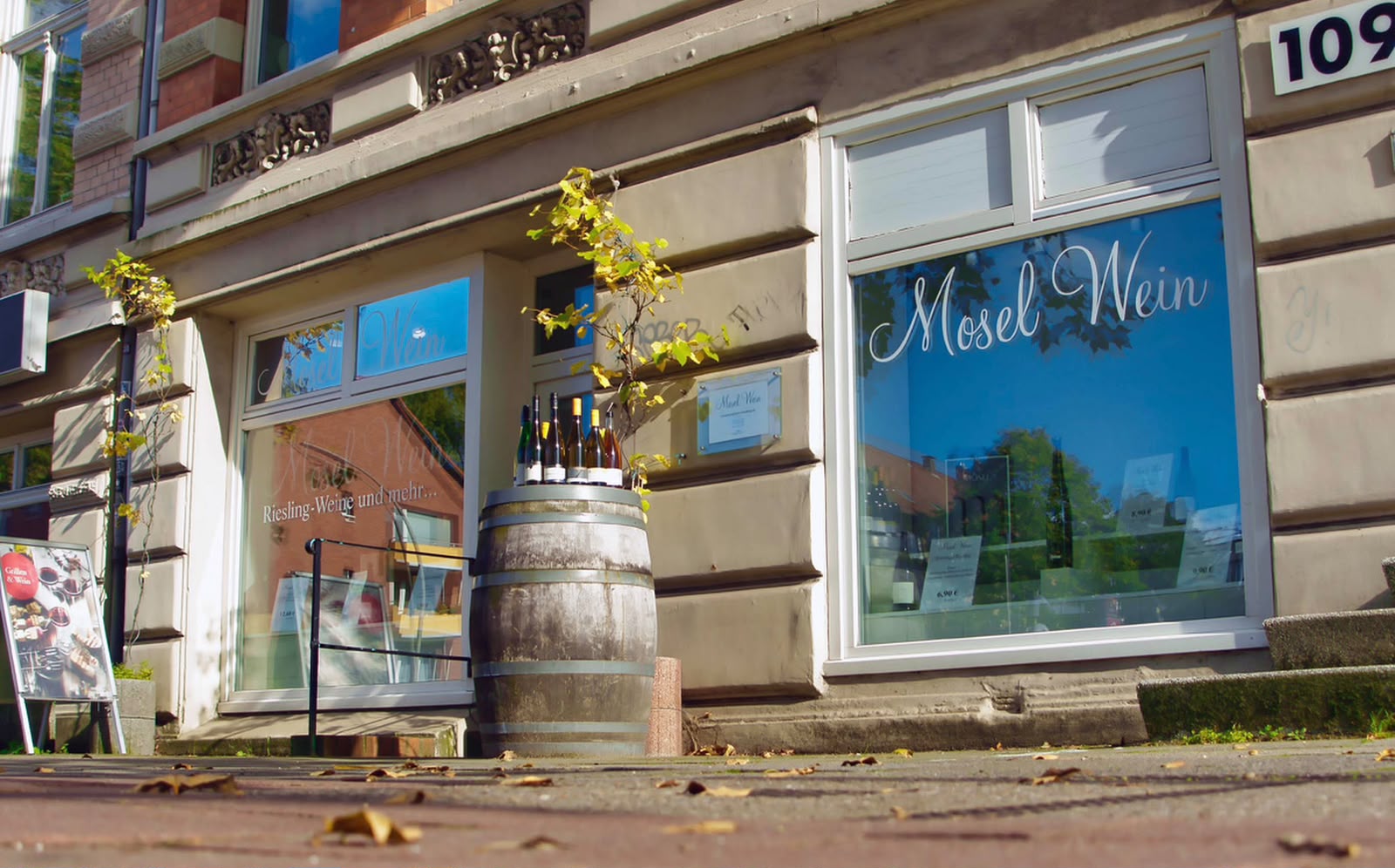 Einladende Außenansicht von Mosel Wein in der Gärtnerstraße mit Schaufenster, Weinfass und echten Flaschen
